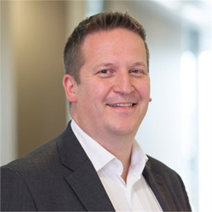 Niall Innes in a dark jacket and white shirt, in front of a window