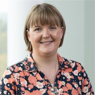 Sarah Jenkins in a black and orange floral top, in front of a window