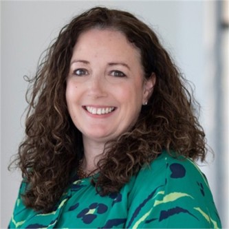 Carol Dick in a green patterned top, in front of a pale background
