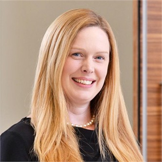 Wendy Ovenden wearing a pearl necklace, black top in front of a brown background.