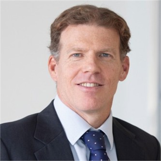 Jonathan Colclough in a dark suit and blue tie, in front of a pale background