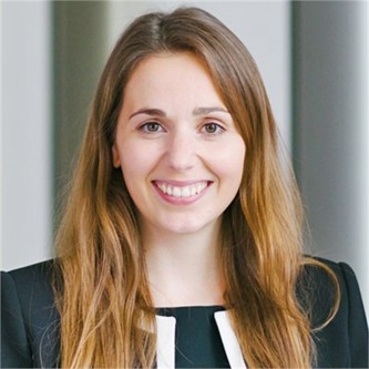 Katherine Wackett in a black jacket with white lapels, in front of a grey background